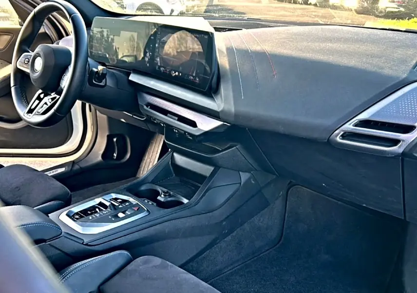 Intérieur BMW Série 1 2025 vu côté passager, tableau de bord et console centrale en tissu noir avec coutures bleues.