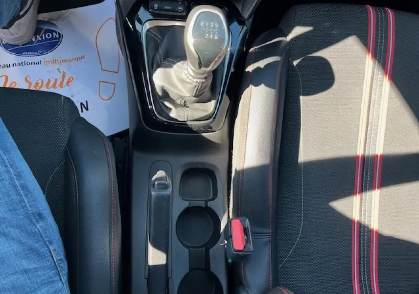 Vue plongeante sur la console centrale d'une Opel Corsa 2021 gris/noir, avec levier de vitesse manuel et sièges sport rayés rouges.