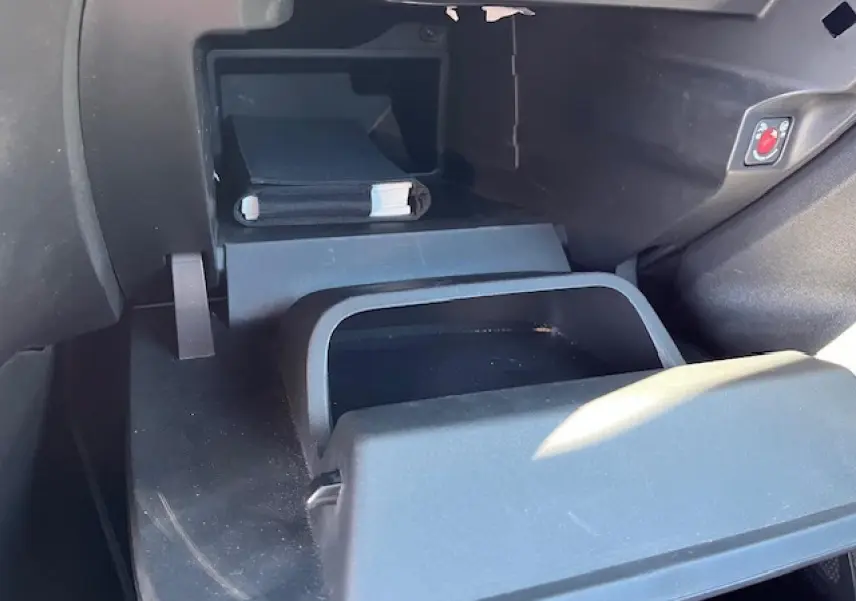 Intérieur de la boîte à gants ouverte de l’Opel Corsa gris/noir, montrant un rangement avec manuel et bouton de sécurité.