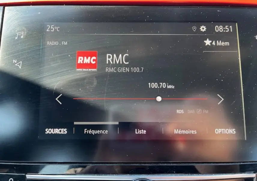 Écran tactile de la radio FM affichant la station RMC 100.7 MHz dans l'habitacle d'une Opel Corsa gris/noir.