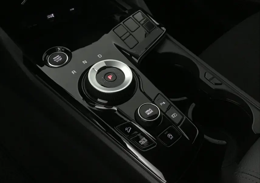 Gros plan sur la console centrale noire brillante du Kia Sportage 2025 avec sélecteur rotatif de boîte auto et bouton start/stop.