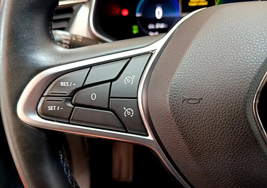 Gros plan sur les commandes de régulateur de vitesse au volant noir du Renault Arkana bleu, tableau de bord numérique en arrière-plan.