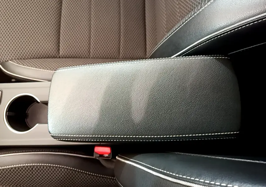 Gros plan sur l'accoudoir central en cuir noir avec surpiqûres blanches, entouré des sièges avant en tissu marron.
