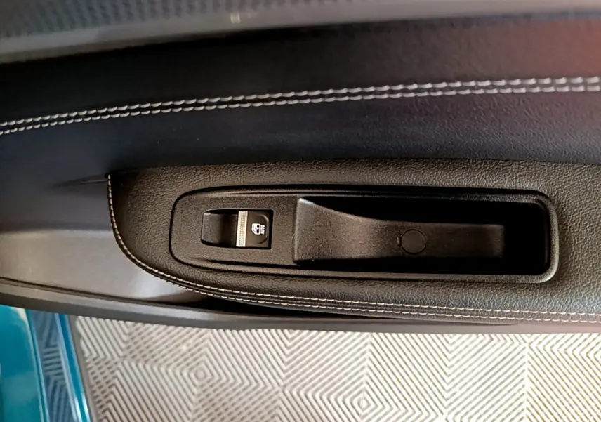 Détail de la poignée intérieure noire avec bouton de verrouillage sur la porte côté gauche d’une Renault Arkana bleu.