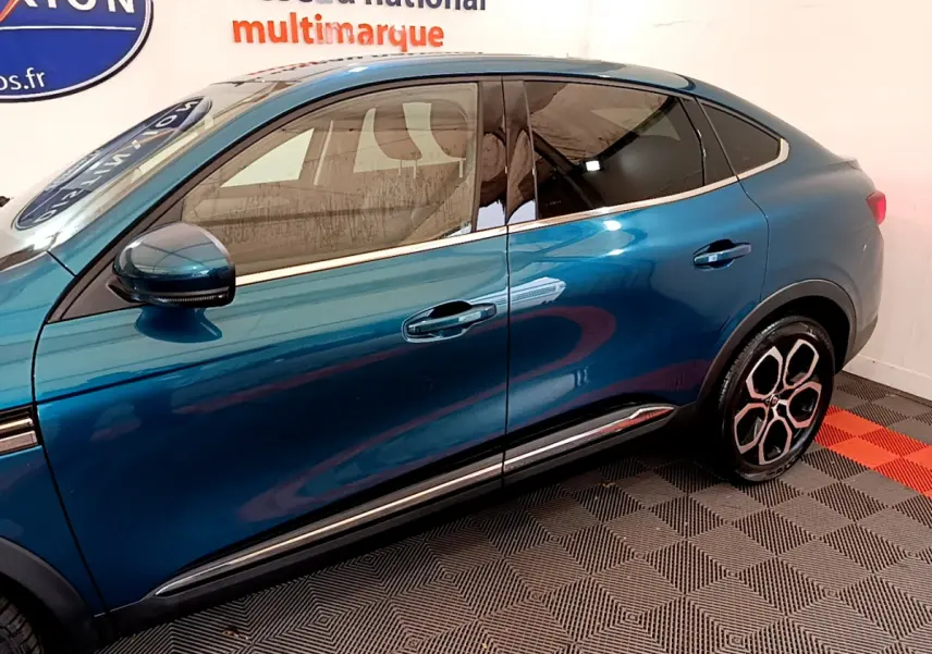 Profil droit du Renault Arkana Techno E-Tech hybride bleu 2023, mettant en valeur ses jantes distinctives et lignes fluides.