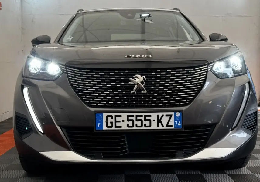 Vue frontale d'un Peugeot 2008 gris foncé 2022 avec phares LED allumés et calandre à motifs chromés.