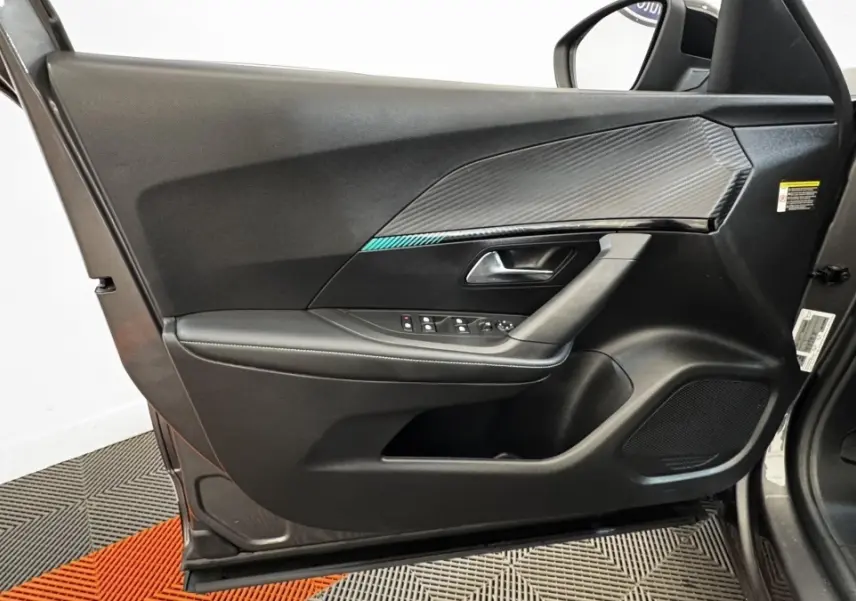 Vue intérieure de la porte avant gauche du Peugeot 2008 gris foncé, avec commandes électriques et insert décoratif noir texturé.