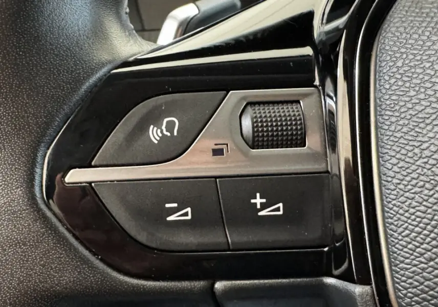 Gros plan sur les commandes vocales et volume du volant cuir noir du Peugeot 2008 gris foncé, version Allure Pack 2022.