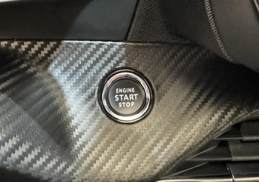 Gros plan sur le bouton start/stop entouré d’un habillage en carbone dans l’habitacle du Peugeot 2008 gris foncé.