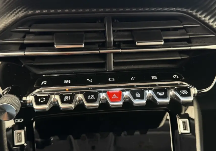 Gros plan sur la console centrale de la Peugeot 2008 gris foncé, mettant en valeur les boutons chromés et l'aération noire.