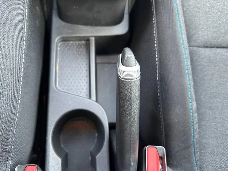 Vue plongeante sur le frein à main manuel et porte-gobelets entre les sièges tissu noir avec surpiqûres bleues du Renault Captur blanc nacré.