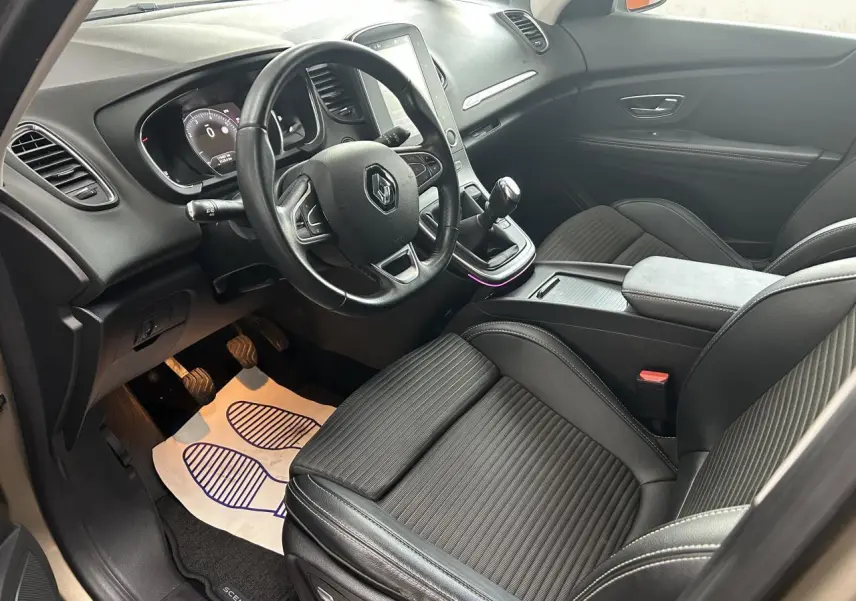Vue intérieure côté conducteur du Renault Scenic Grand IV avec sièges noirs en similicuir et console centrale moderne.