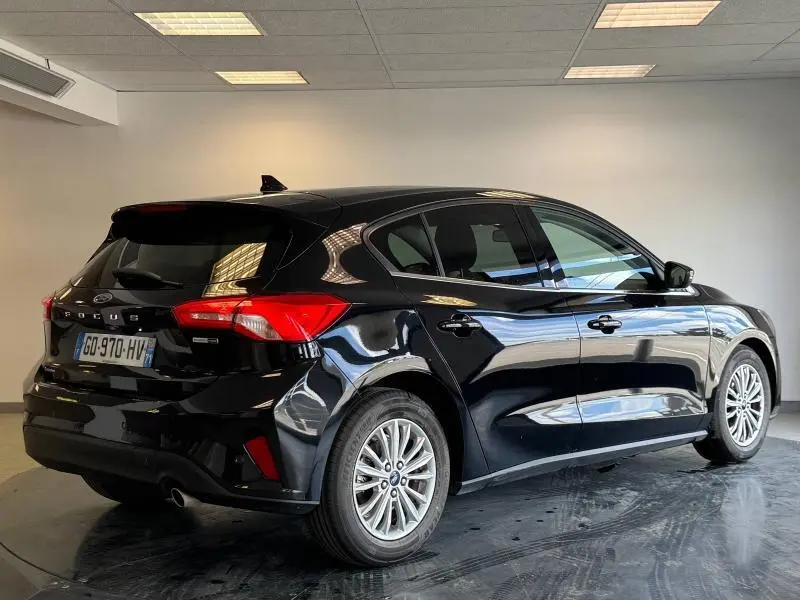 Ford Focus noir Agate métallisé vue 3/4 arrière droit avec feux rouges et jantes alliage en intérieur showroom.