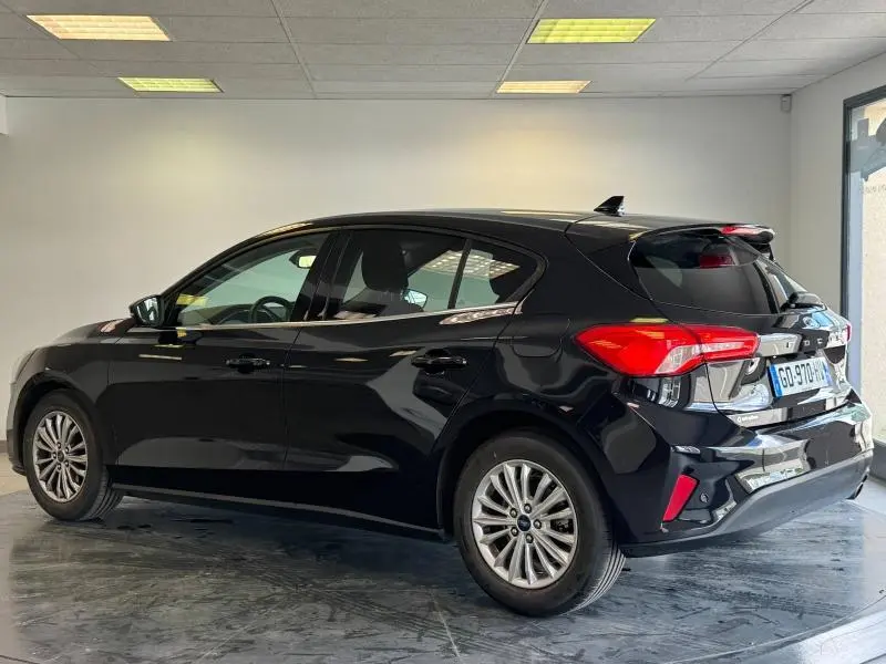 Ford Focus noir Agate métallisé vue 3/4 arrière côté gauche en intérieur avec feux arrière distinctifs rouges.