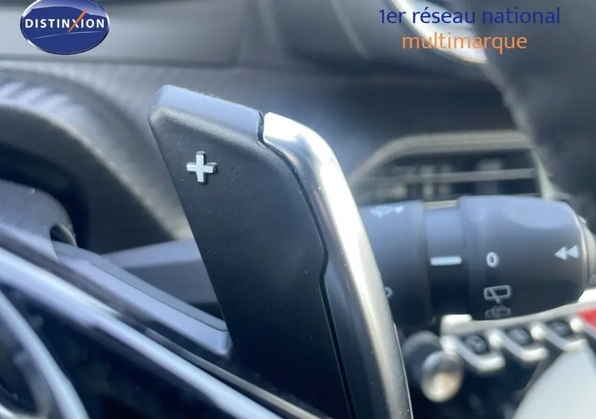 Gros plan sur la palette de changement de vitesse + au volant d'un Peugeot 2008 gris Artense hybride 2025.