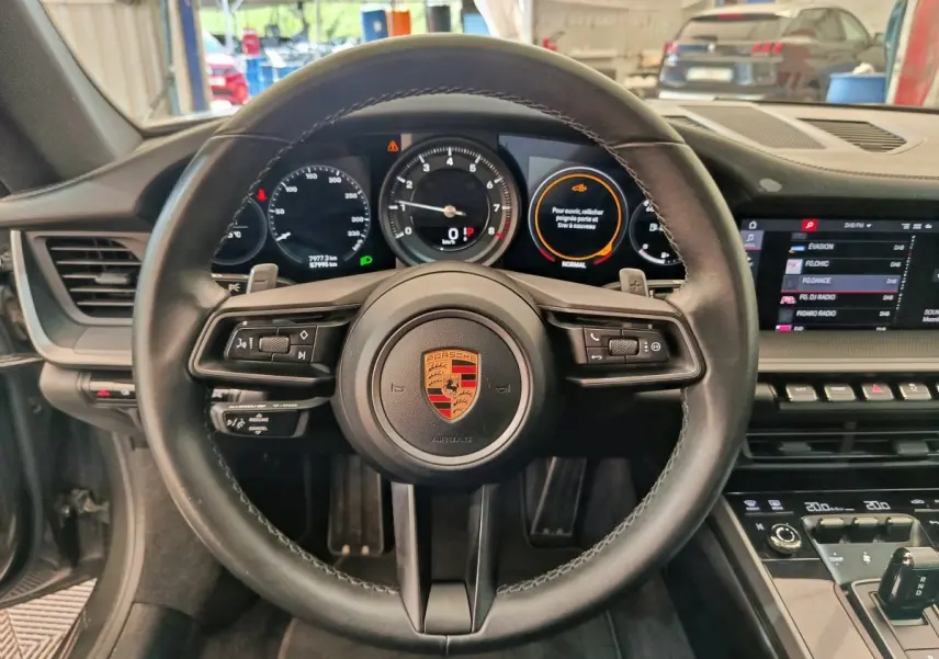 Vue intérieure centrée sur le volant cuir noir de la Porsche 911 Carrera 4S avec tableau de bord numérique et écran tactile.