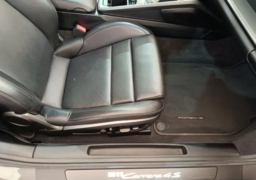Vue intérieure côté conducteur sur le siège en cuir noir et tapis de sol Porsche d'une 911 Carrera 4S Coupé gris foncé.