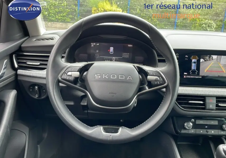 Vue intérieure centrée sur le volant SKODA d'une Scala 2025, avec tableau de bord numérique et écran de caméra de recul.