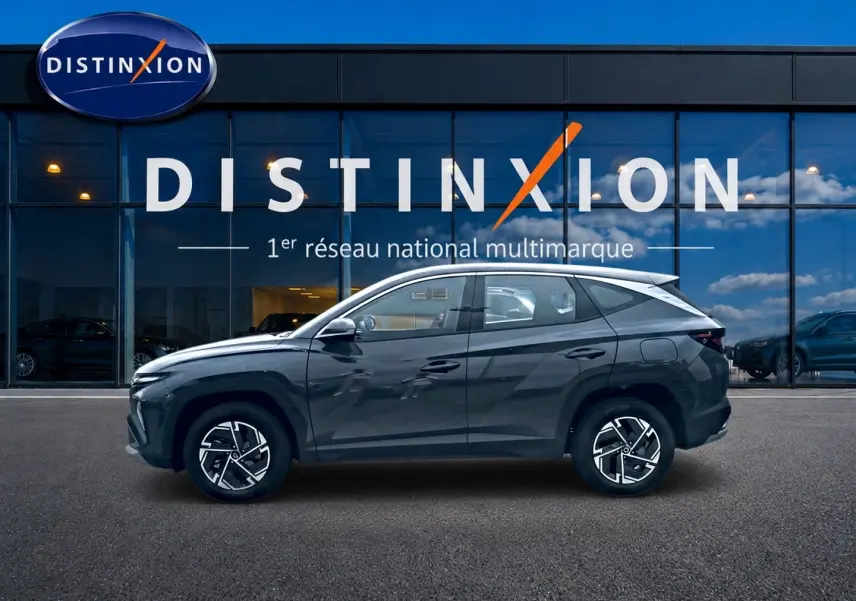 Vue de profil côté gauche du Hyundai Tucson 1.6 t-gdi 239 hybride gris ecotronique devant une vitrine Distinxion.