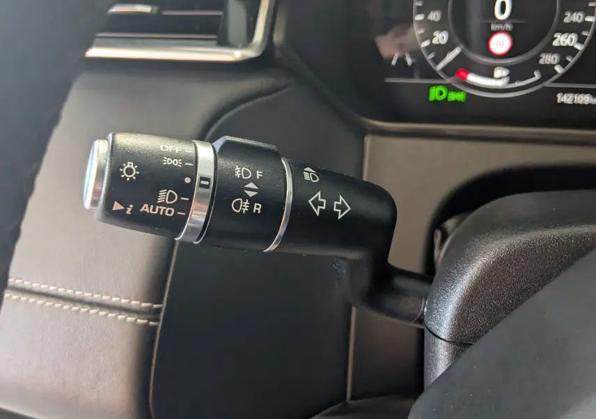 Gros plan sur la commande des feux et clignotants du Range Rover Velar noir, tableau de bord digital en arrière-plan.