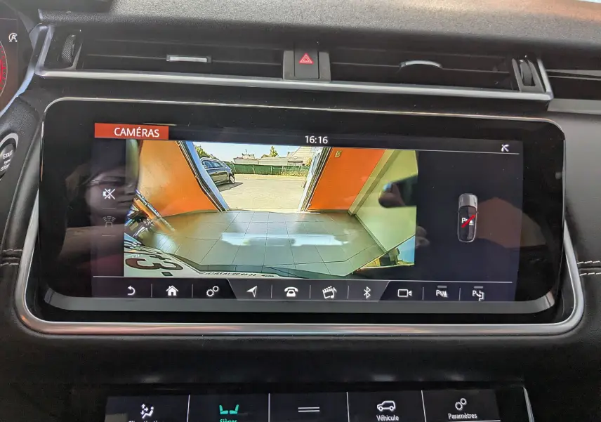 Écran central du Range Rover Velar noir montrant la caméra de recul avec vue sur un garage et l'extérieur.