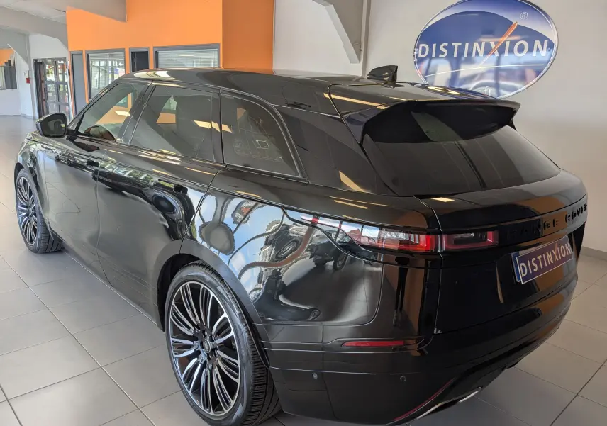 Vue 3/4 arrière droite d'un Range Rover Velar noir brillant avec jantes alliage et vitres teintées en intérieur showroom.