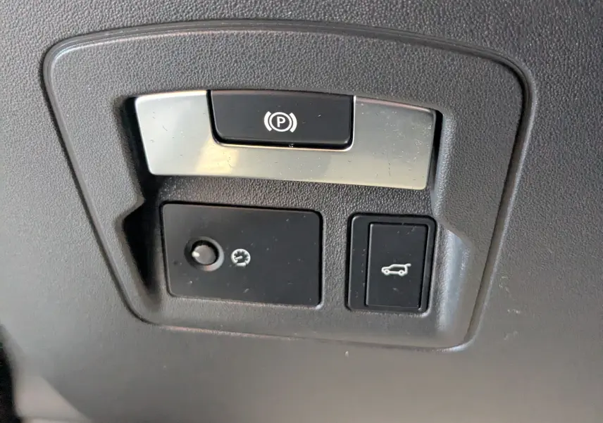 Gros plan sur les commandes de frein à main électronique et ouverture du coffre dans un Range Rover Velar noir 2020.