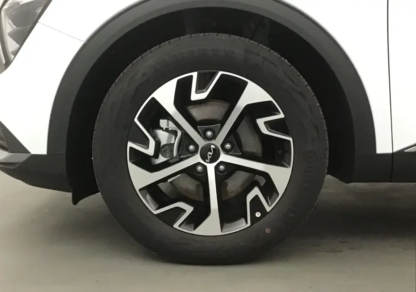 Gros plan sur la roue avant gauche du Kia Sportage blanc 2025 avec jante alliage noire et argentée au design moderne.