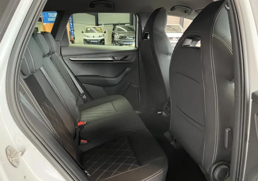 Vue intérieure côté gauche sur la banquette arrière noire avec surpiqûres blanches du Skoda Karoq Sportline blanc 2025.