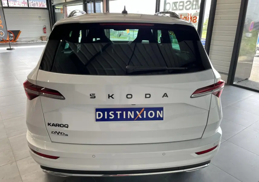 Vue arrière d'un SUV SKODA KAROQ blanc 2025 avec logo SKODA et hayon fermé en intérieur showroom.