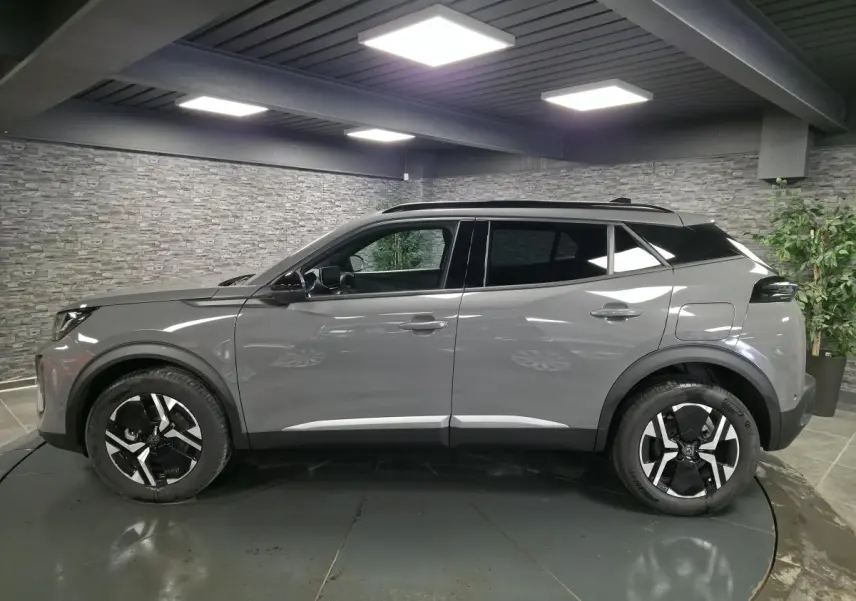 Vue de profil côté gauche d'un Peugeot 2008 gris métallisé avec jantes alliage bi-ton noir et toit noir dans un intérieur showroom.