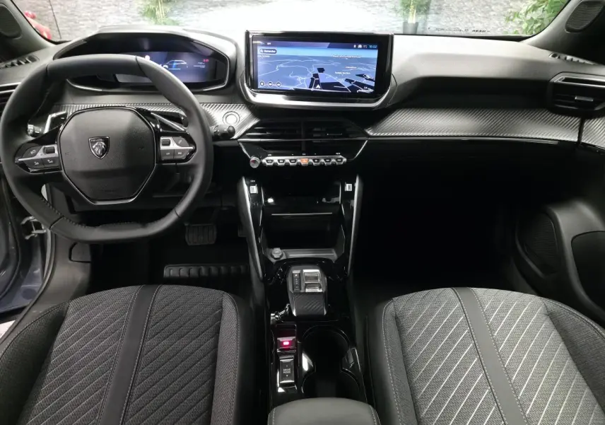 Vue intérieure avant du Peugeot 2008 1.2i Hybrid 2025, tableau de bord carbone et écran tactile central.