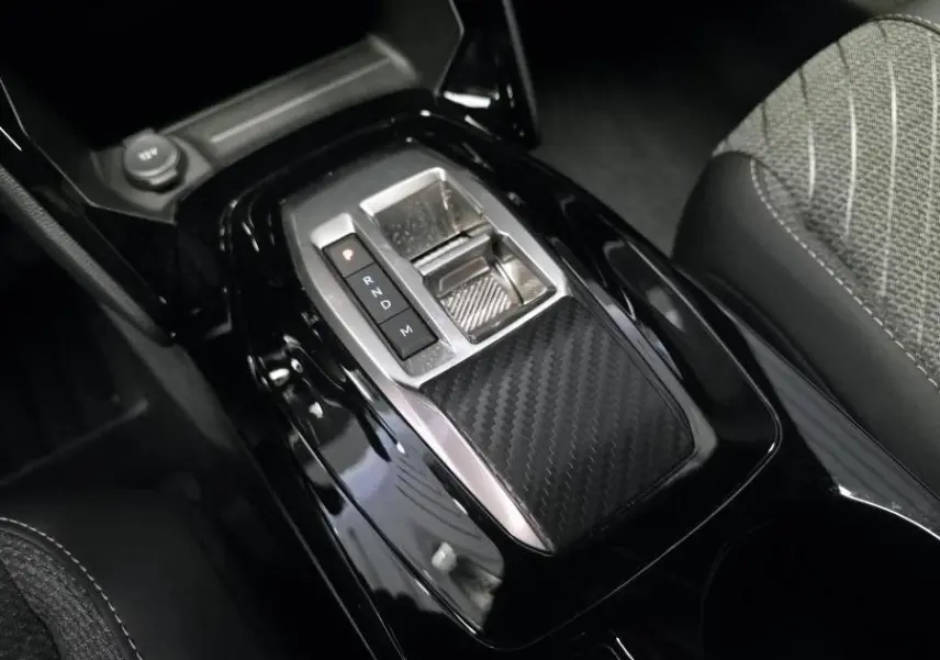 Gros plan sur la console centrale noire brillante avec sélecteur de boîte automatique et décor carbone du Peugeot 2008 gris.