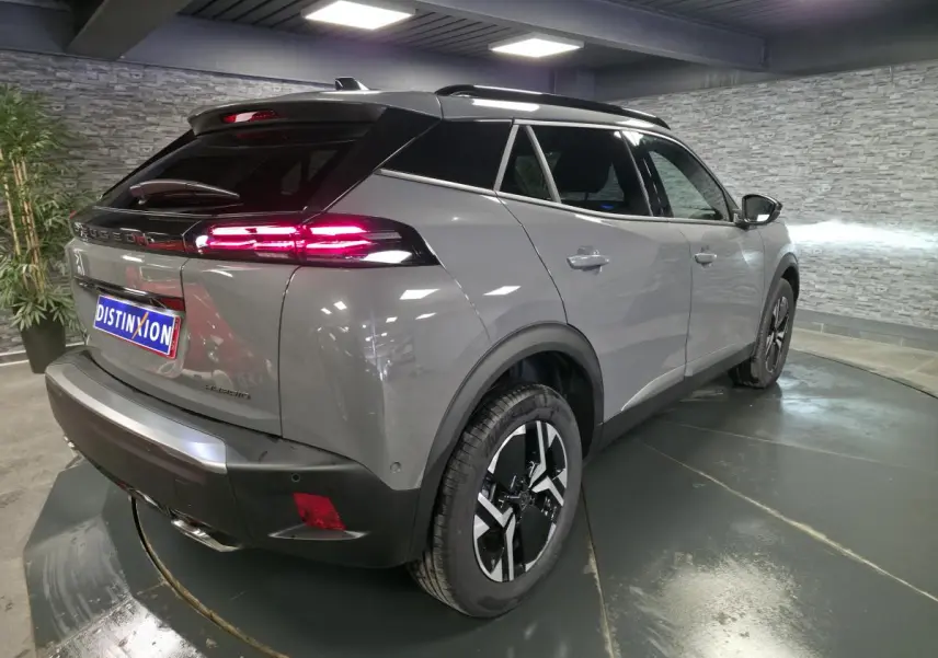 Vue 3/4 arrière droite du Peugeot 2008 gris avec toit noir et feux arrière LED allumés en intérieur showroom.