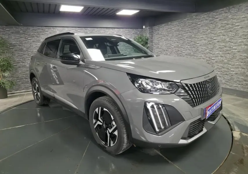 Peugeot 2008 gris en 3/4 avant droit, avec calandre noire à marquages verticaux et feux LED 3 griffes.