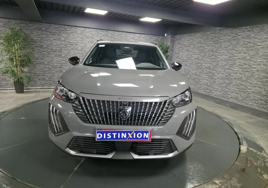 Vue frontale d'un Peugeot 2008 gris métallisé avec calandre verticale et feux LED en griffes, en intérieur showroom.