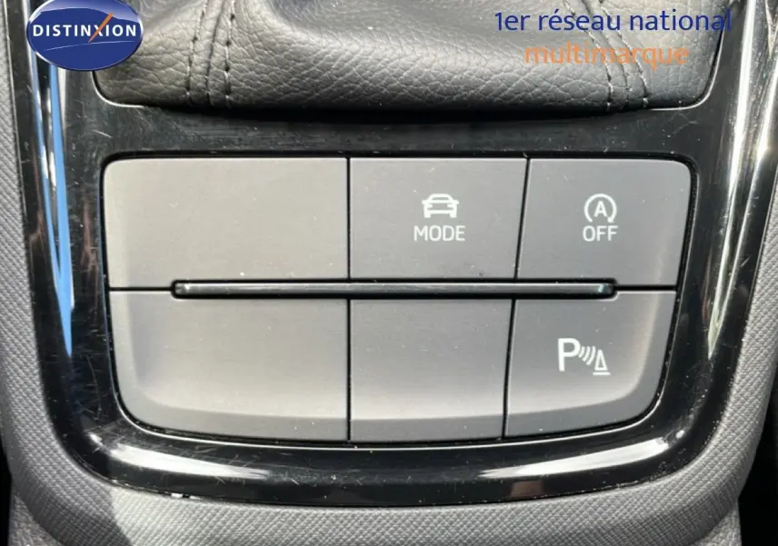 Gros plan sur les boutons de commande du mode de conduite et de l'aide au stationnement dans une Skoda Scala blanc glacier.