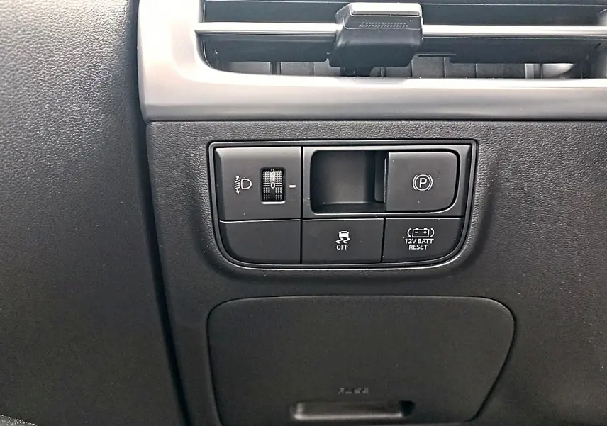 Gros plan sur les commandes noires du tableau de bord du Hyundai Tucson gris, avec réglage des phares et frein de stationnement électrique.