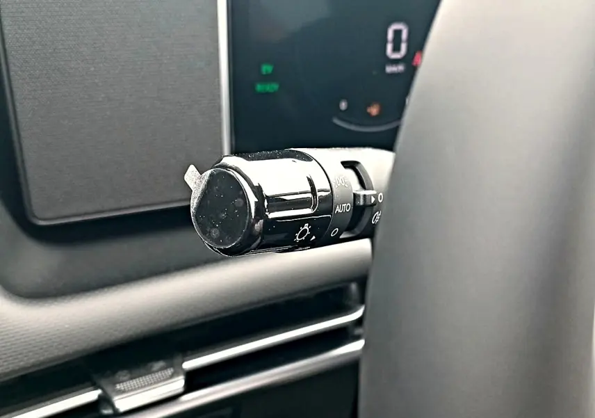 Gros plan sur la commande des phares noire à gauche du volant dans l’habitacle du Hyundai Tucson gris ecotronique 2026.