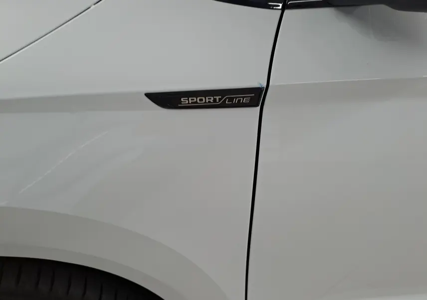 Gros plan sur l'aile avant gauche blanche lune du Skoda Karoq 2025 avec logo Sportline noir.