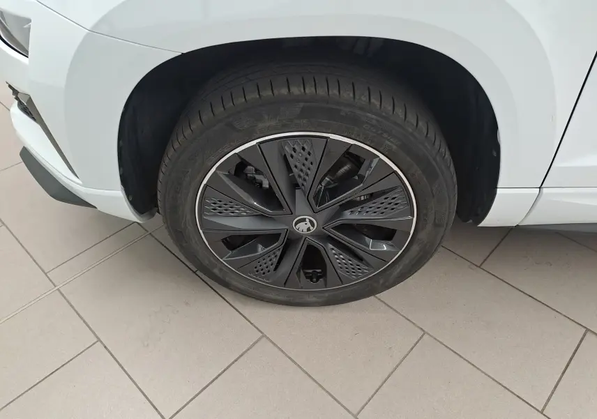 Gros plan sur la roue avant droite d'un Skoda Karoq blanc lune avec jante noire au design moderne.