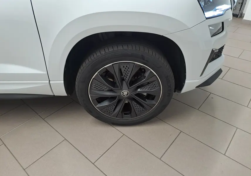 Gros plan sur la roue avant droite noire et argentée du Skoda Karoq blanc Lune, avec partie avant du véhicule visible.
