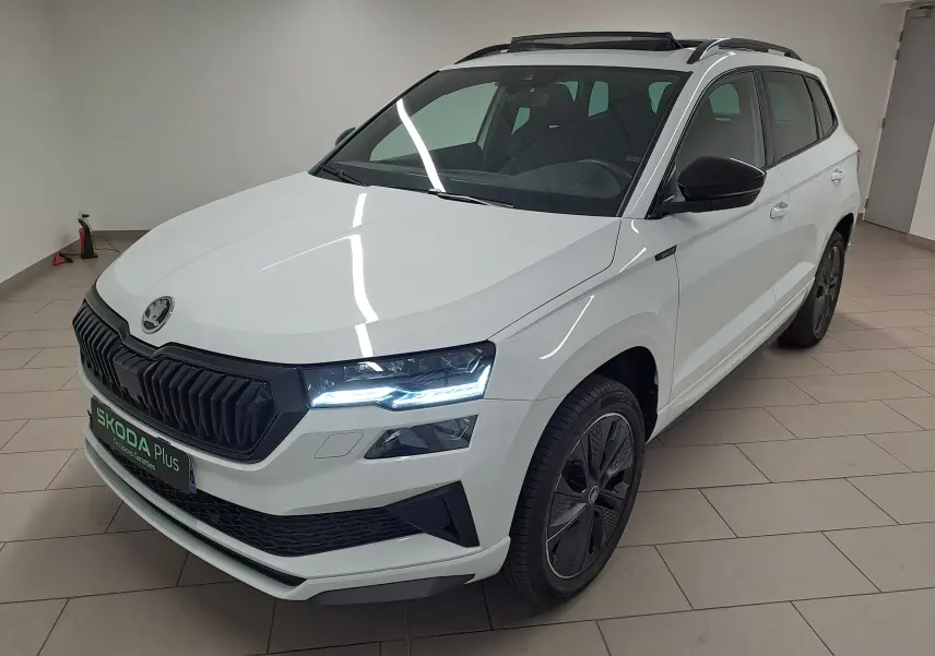 Vue 3/4 avant droite d'un Skoda Karoq blanc lune avec toit ouvrant panoramique et calandre noire sportive.
