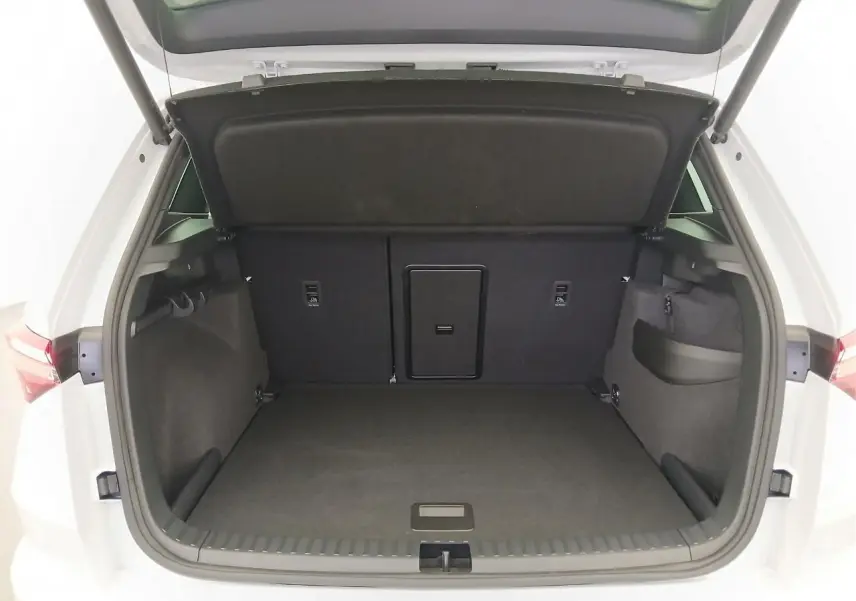 Coffre ouvert vu de l'arrière d'un Skoda Karoq blanc lune, montrant un espace de chargement spacieux et propre.