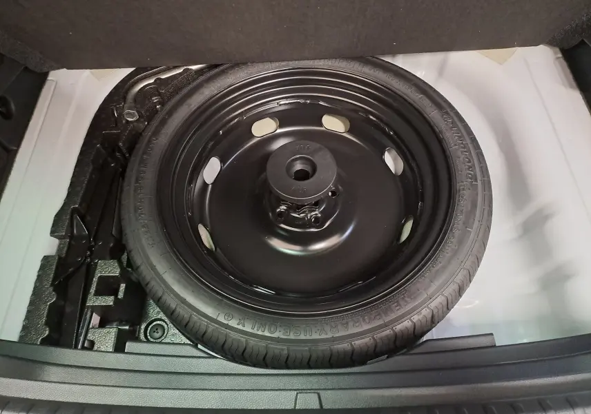 Gros plan sur la roue de secours galette noire dans le coffre blanc lune du Skoda Karoq 2025.