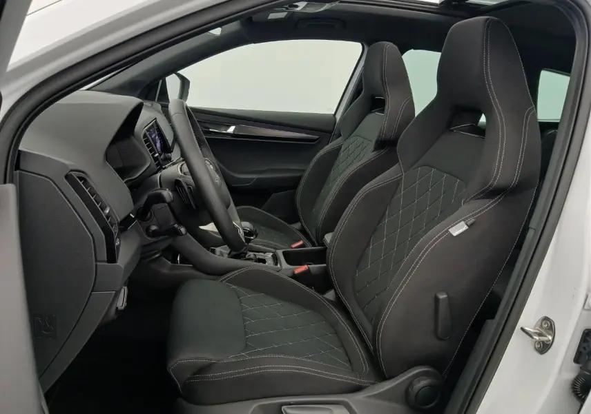 Vue intérieure côté conducteur du Skoda Karoq blanc lune 2025, sièges sport noirs avec surpiqûres blanches.