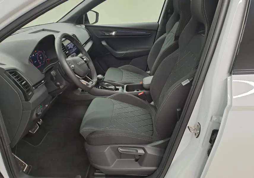 Vue intérieure côté conducteur du Skoda Karoq blanc lune 2025, sièges sport noirs avec surpiqûres contrastées.