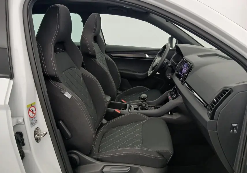 Vue intérieure côté conducteur du Skoda Karoq blanc lune 2025, sièges sport noirs avec surpiqûres blanches.