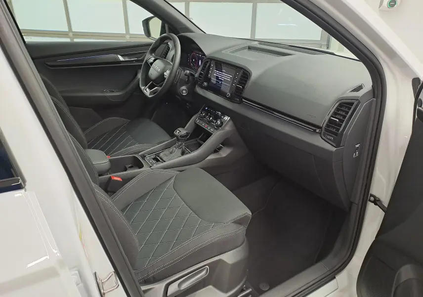 Vue intérieure côté conducteur du Skoda Karoq blanc lune 2025, avec sièges noirs et tableau de bord moderne.