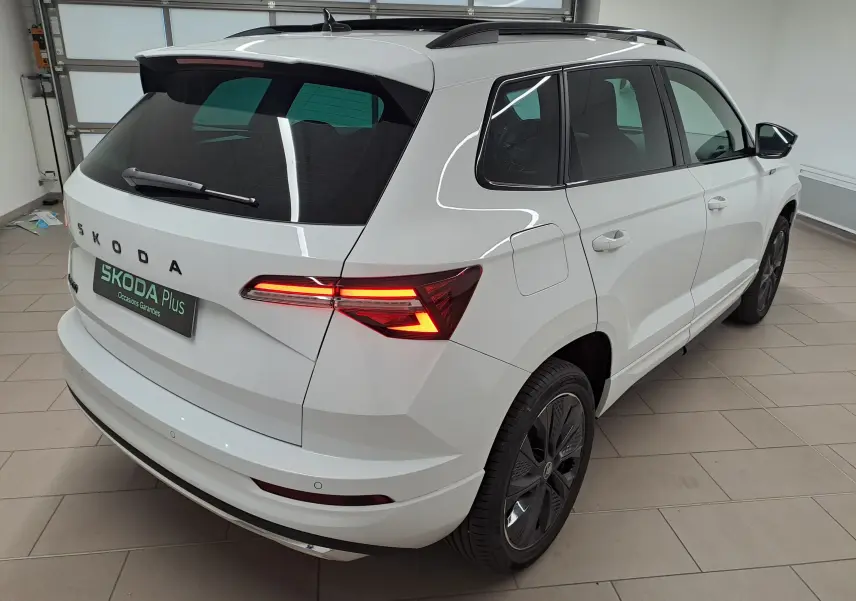 Vue 3/4 arrière droite du Skoda Karoq blanc Lune avec feux arrière allumés et toit panoramique fermé.